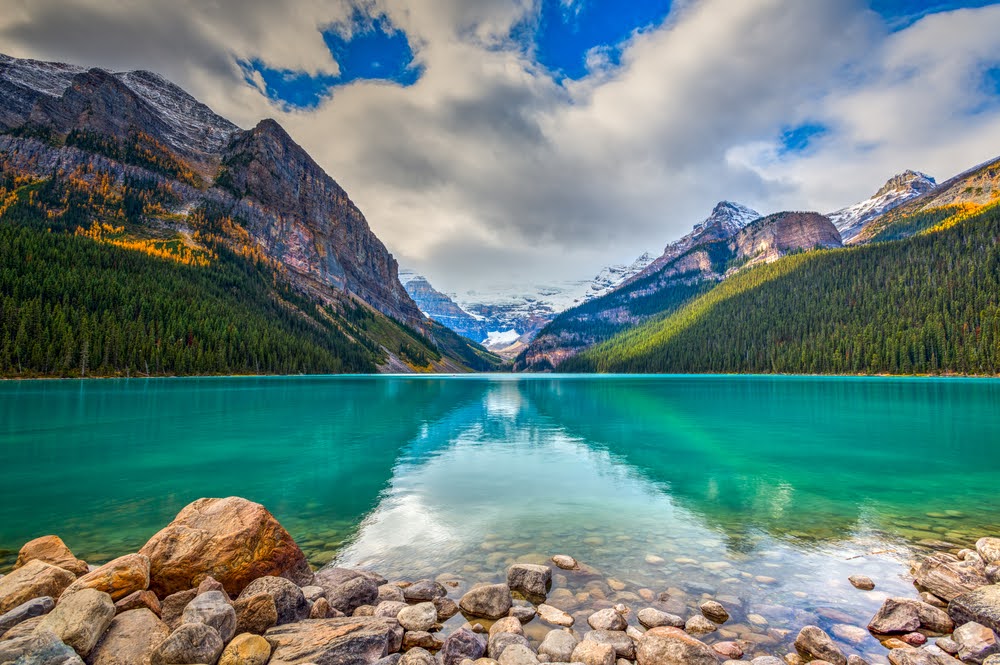 View of Lake Louise with rocks in front with mountains and trees in the background