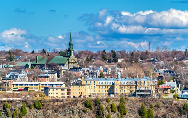 A Canadian town under a blue sky with white clouds in the distance. The buildings are mostly yellow, with a grey church with a green roof.