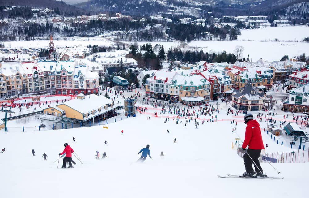 Skiers going down a snowy slope heading towards Mont Tremblant resort with a landscape view in the background.