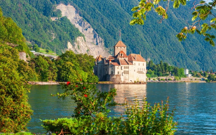 A blue lake, green mountain slopes and a small castle in Montreux.