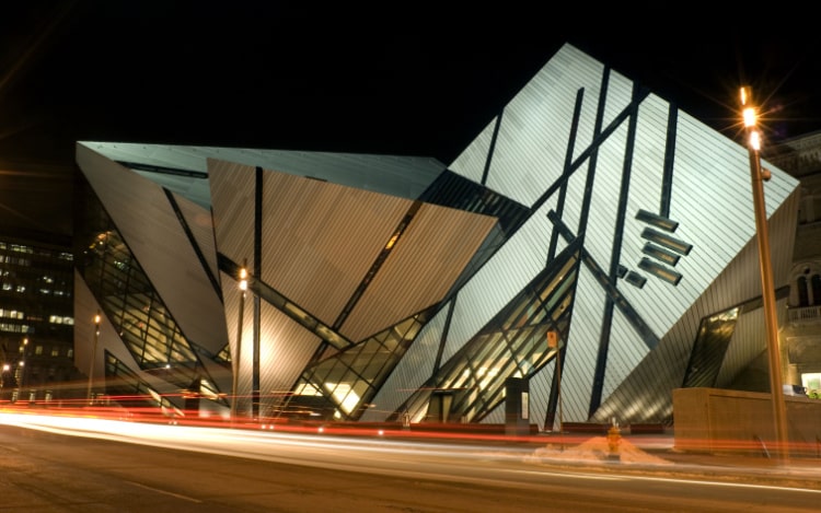 The exterior of Toronto’s Royal Ontario Museum at night, a building with several protruding corners and leaning windows.