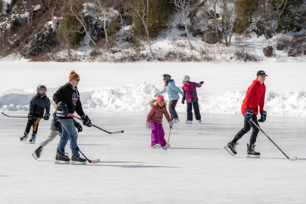 People ice skating with hockey sticks with snow in the background