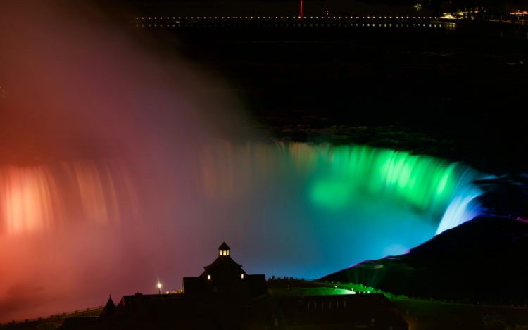 Niagara Falls at night, illuminated by lights in multiple colours including red, green and blue.