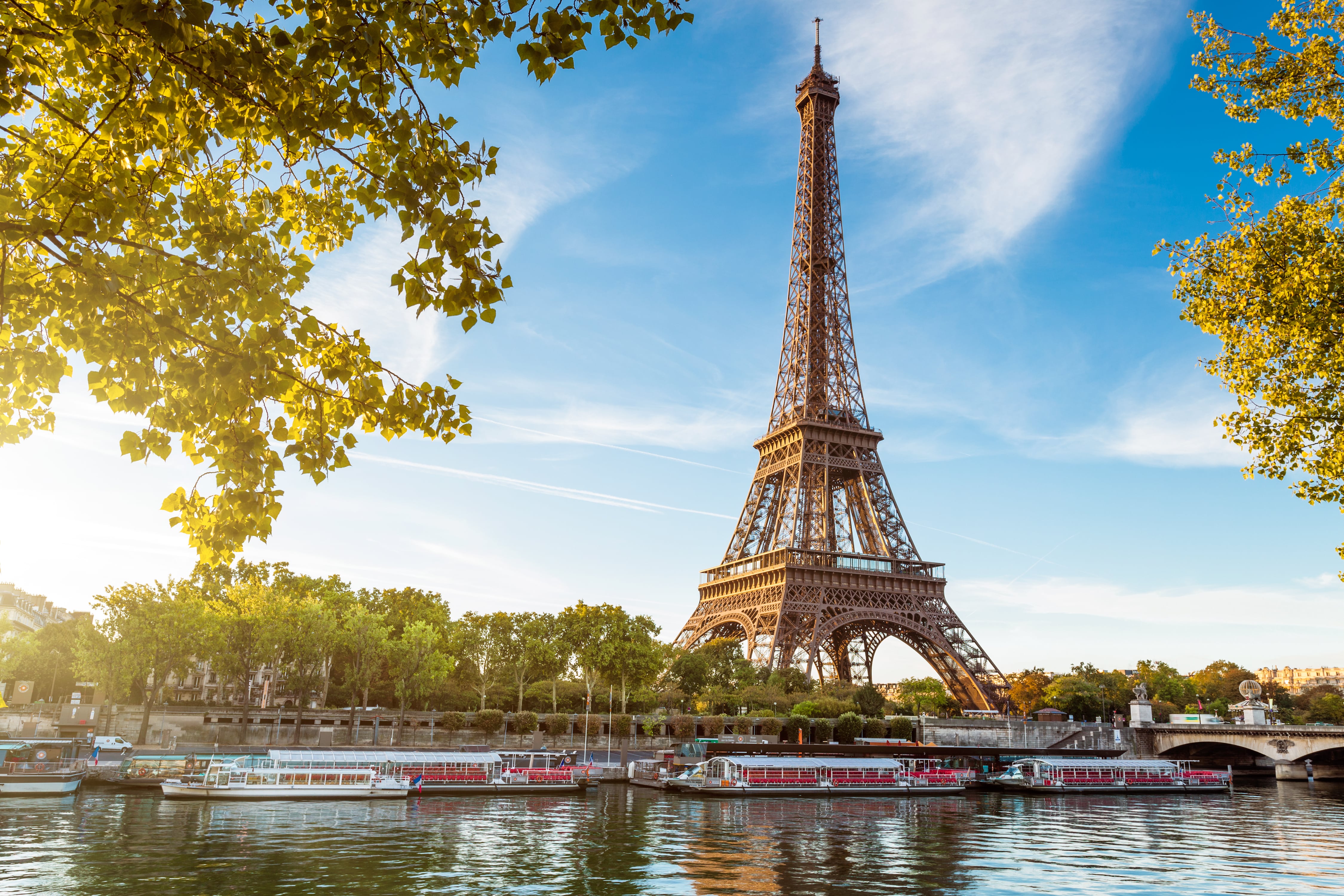 Picture of the Eiffel Tower taken at sunset with the Seine river and boats in front of it