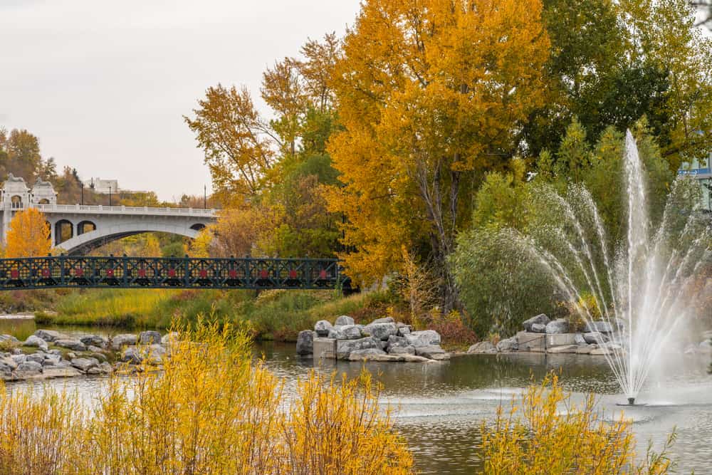 A river bank with Autumn foliage, rocks, a fountain and two bridges