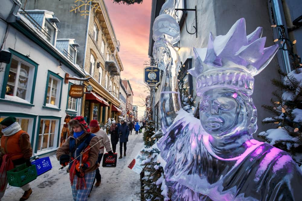 People walking down a narrow street with an ice sculpture on the right