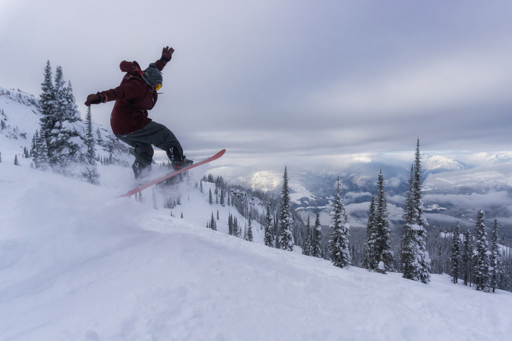 Snowboarder riding down snowy slopes on a cloudy evening with trees in the background