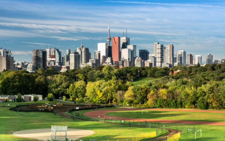 A view of the Toronto city skyline from Riverdale Park. The grass in the park is neatly cut and has a red track running through it. 