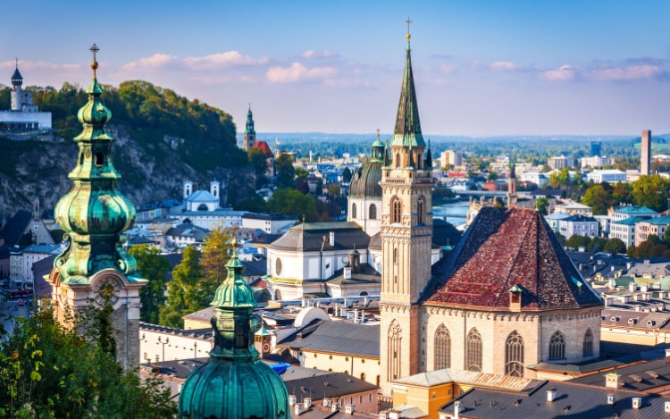 A high-up view of Salzburg’s buildings, including green spires and a church.