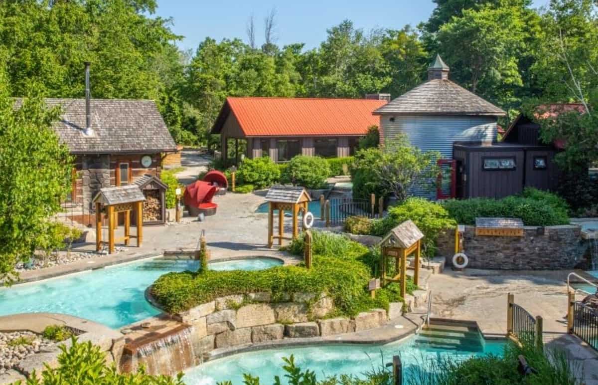 Two pools in front with paths leading to spa buildings and trees surrounding the area