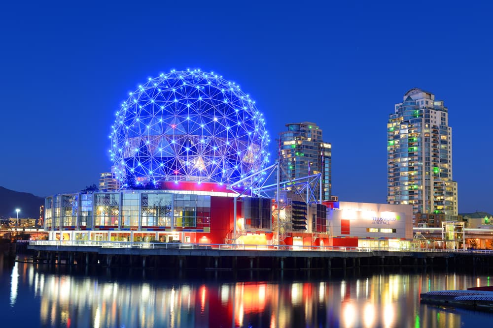 Science World lit up at night next to two other tall buildings and a waterfront