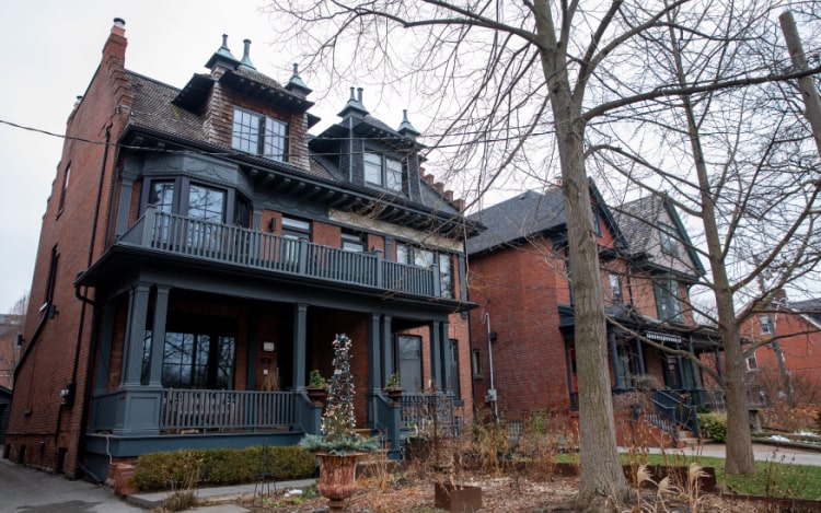 A large red brick detached house with a dark blue porch and a dark blue balcony. Two bare trees are on the right of the image.