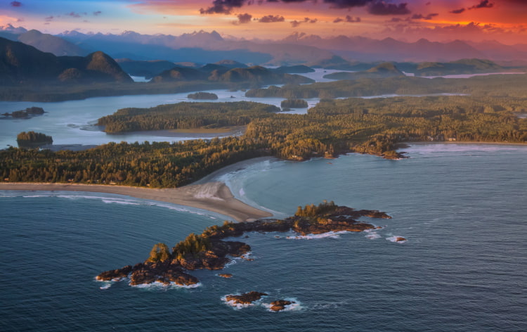 Aerial view of Canadian coastline at sunset, with trees and sand meeting blue water and an orange-red sky above