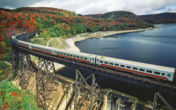 A white train going over a railway bridge above a lake.