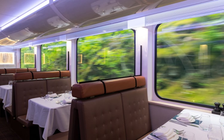 A 1st class train car with brown leather seats and white tablecloths.