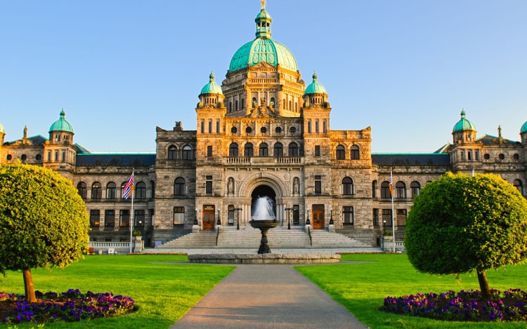 Victoria’s parliament building made of stone with teal domes on top, under a blue sky.