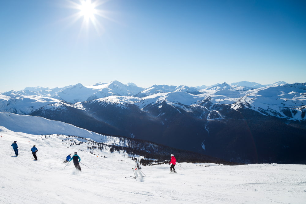 People skiing down a snowy mountain with other snow-capped mountains in the background