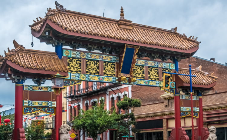 The entrance to Vancouver’s Chinatown, which is a large gate with sloped terracotta roofing, yellow and blue dragons running across its frame, and red painted posts holding it up.