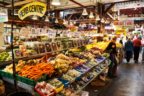 A vibrant market stall showcasing fruit and vegetables. In the distance, you can see shoppers browsing other stalls.
