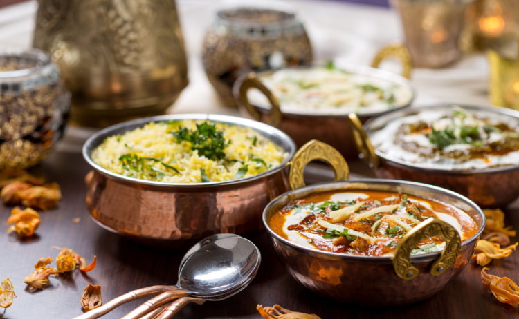 Two copper dishes - the one on the left is filled with a mound of yellow pilau rice topped with coriander and the dish on the right is filled with an orange-brown curry and a swirl of white sauce