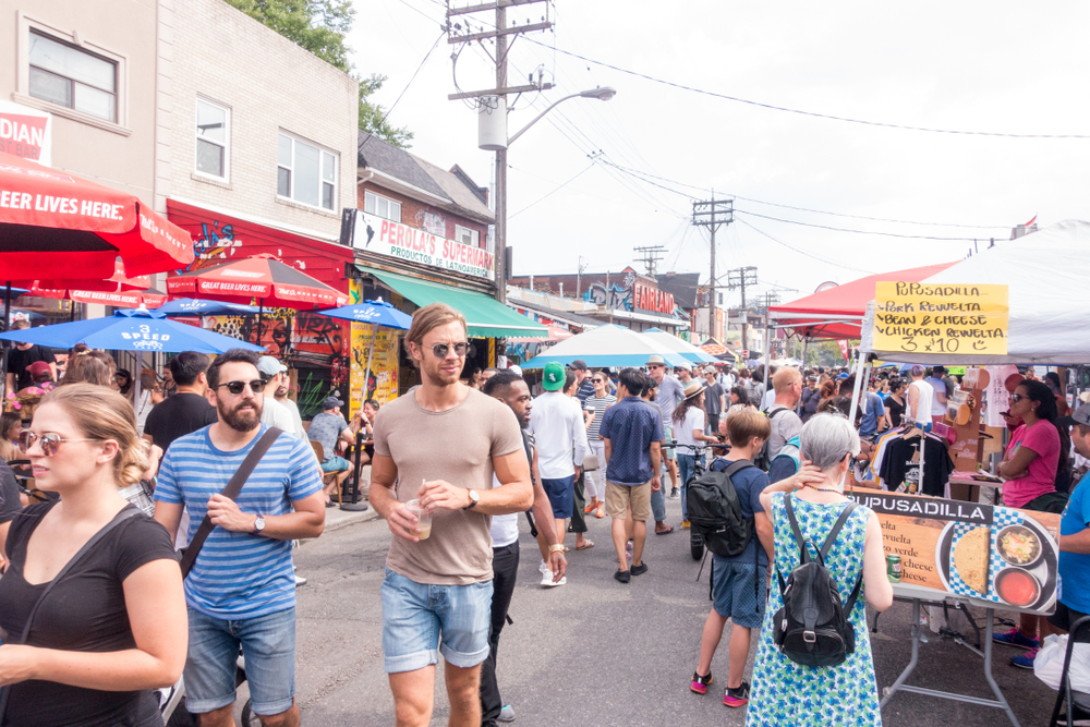 A view of Kensington Market. The streets are filled with shoppers and stalls on a warm summer’s day.