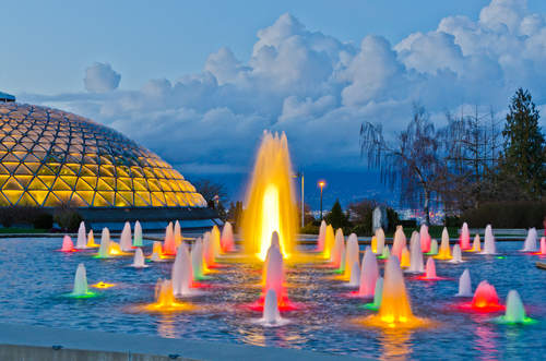 A water fountain at Queen Elizabeth Park. The sun is setting, and there are lights of multiple colours coming out of the water fountain
