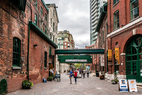 The Distillery District in Toronto. People can be seen walking between the red brick buildings in the daytime.