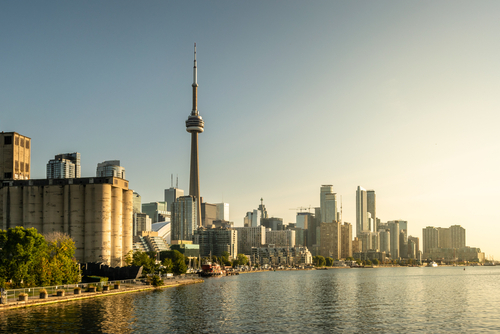 A shot of the Toronto skyline. There is a tower in the centre of the shot, the sun is rising and you can see the shoreline.